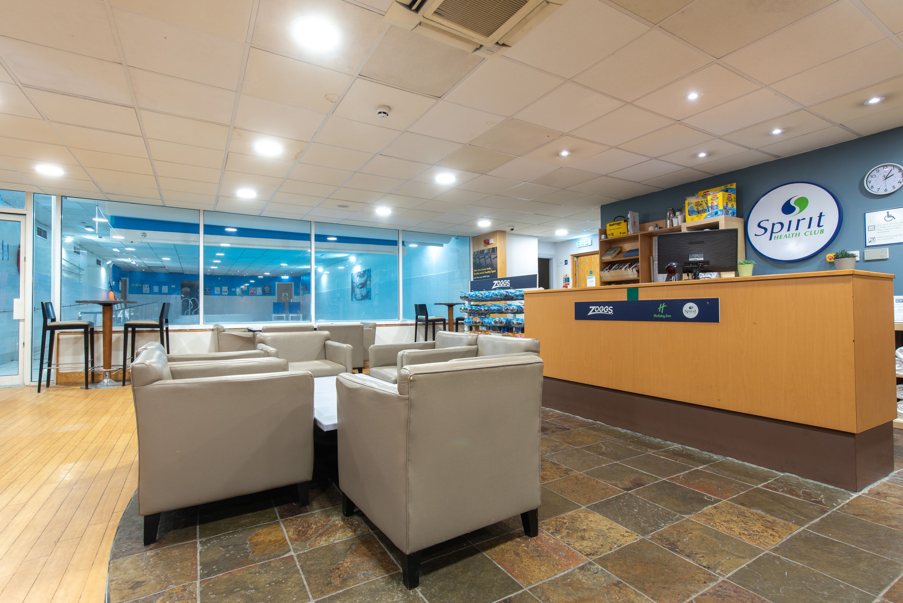 A reception area with a wooden desk, beige sofas, and a blue wall with a 'Spirit Health Club' sign.