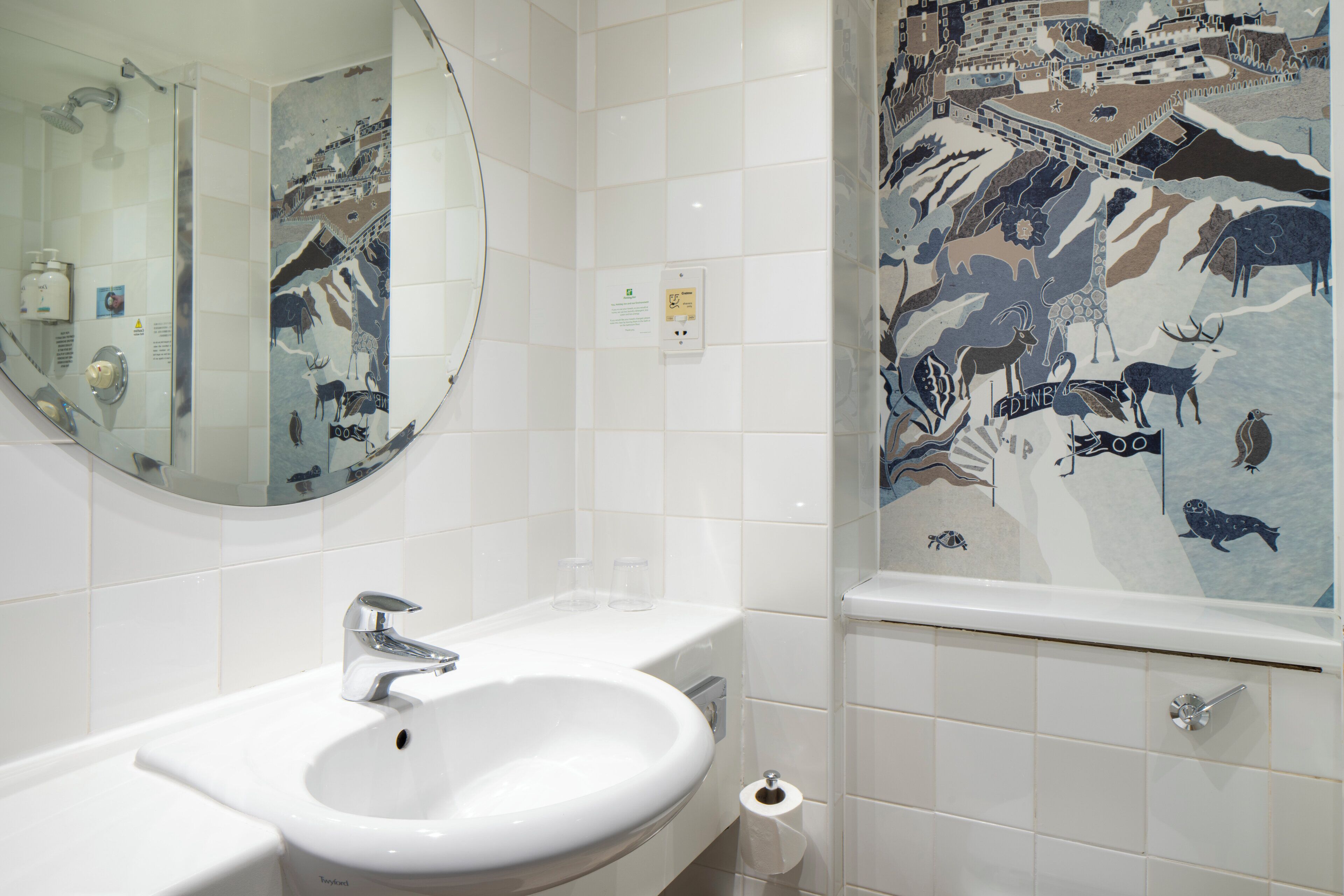 Une salle de bain avec un lavabo blanc, un miroir et des murs carrelés.