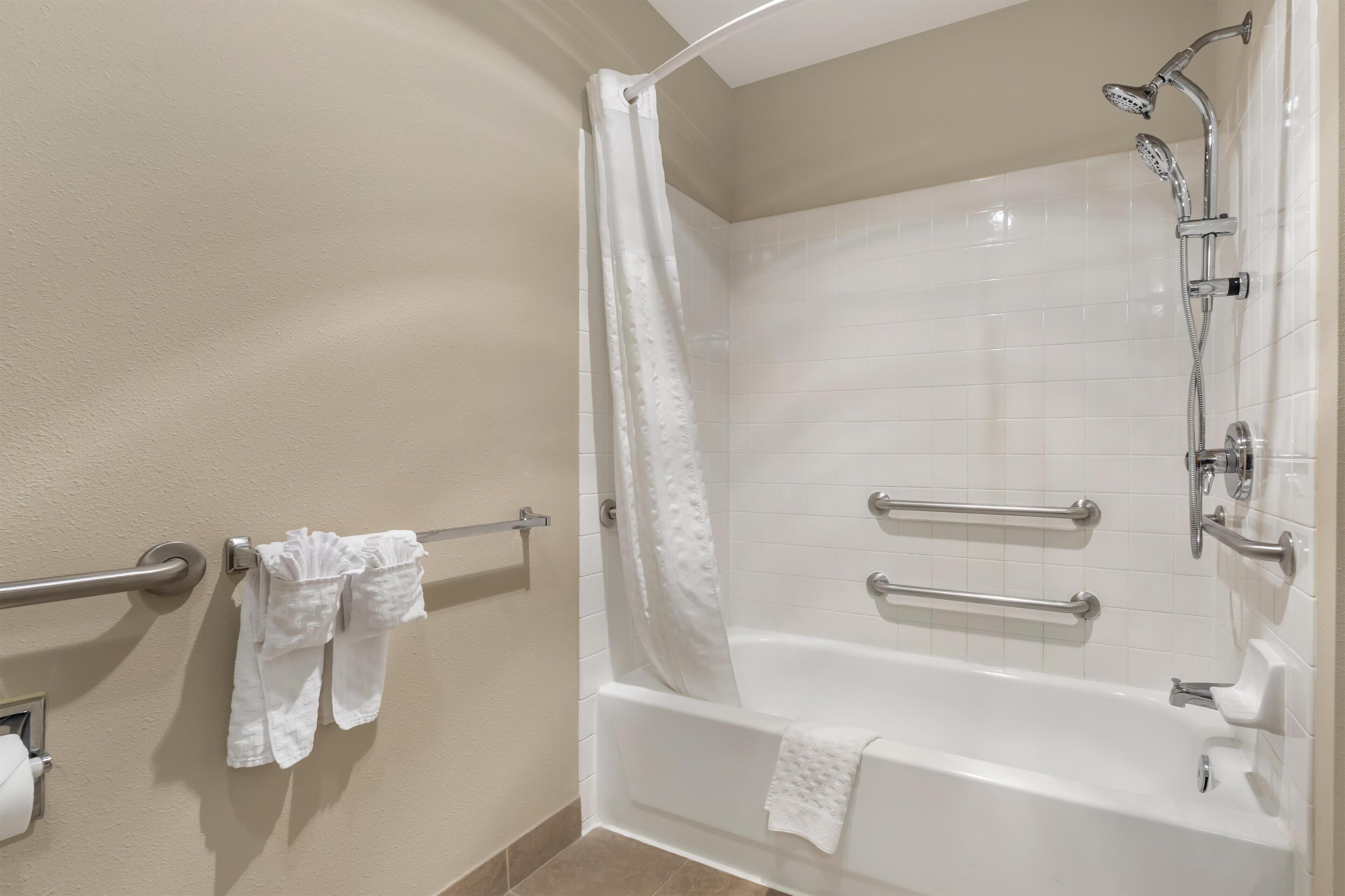 A bathroom with a white bathtub, a shower, and grab bars. There are towels hanging on a rack.