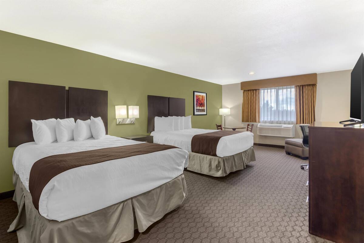 A hotel room with two beds, a desk, a chair, a TV, and a window with curtains.