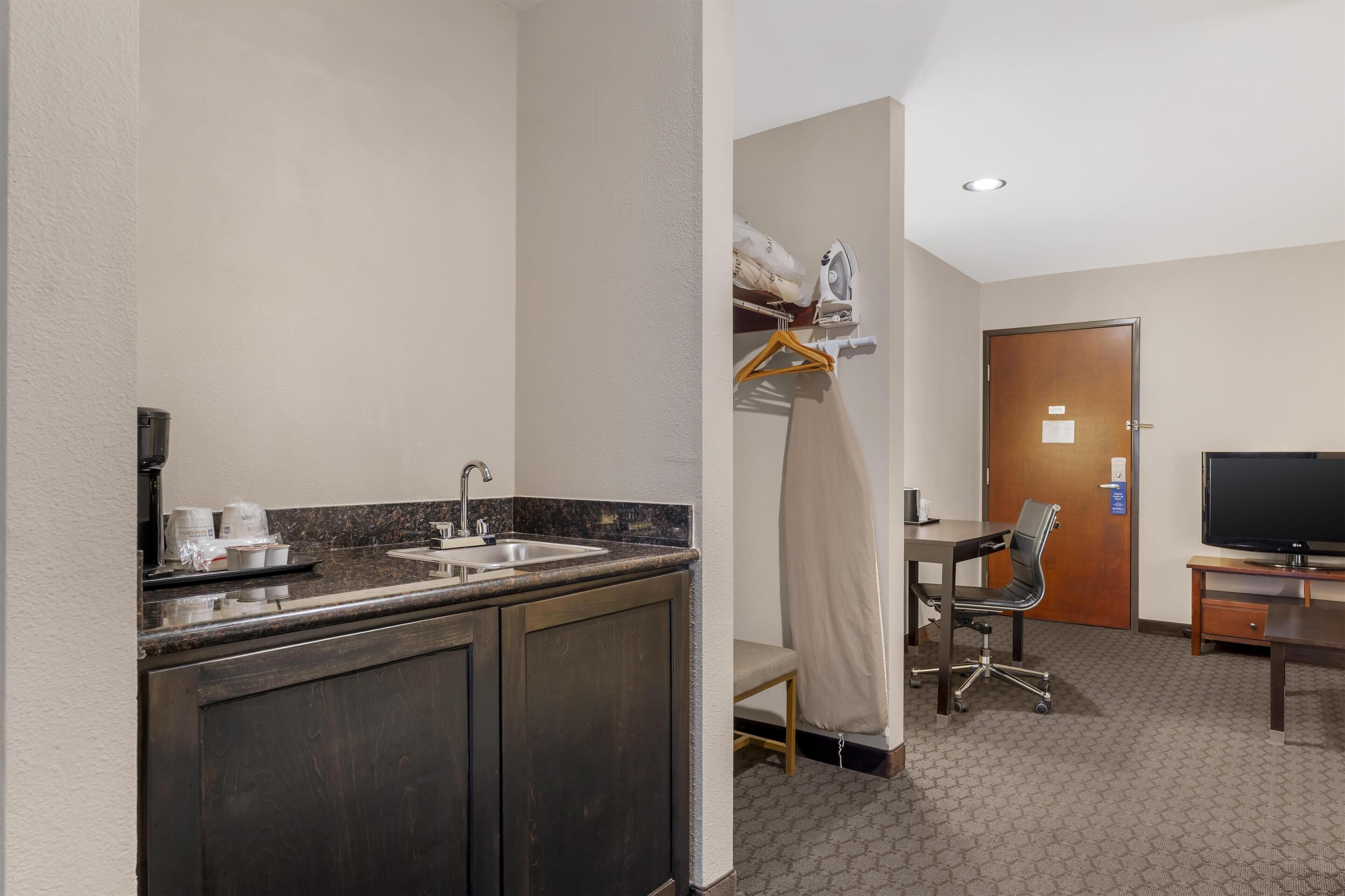 A hotel room with a kitchenette, a desk with a chair, a television, and a shower area.