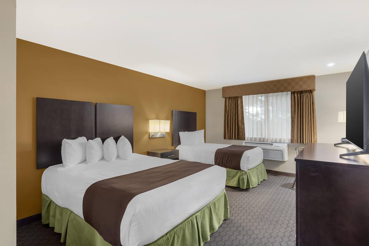 A hotel room with two beds, a desk, a TV, and a window with curtains.