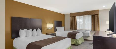 Ein Hotelzimmer mit zwei Betten, einem Schreibtisch, einem Fernseher und einem fenster mit Vorhängen.