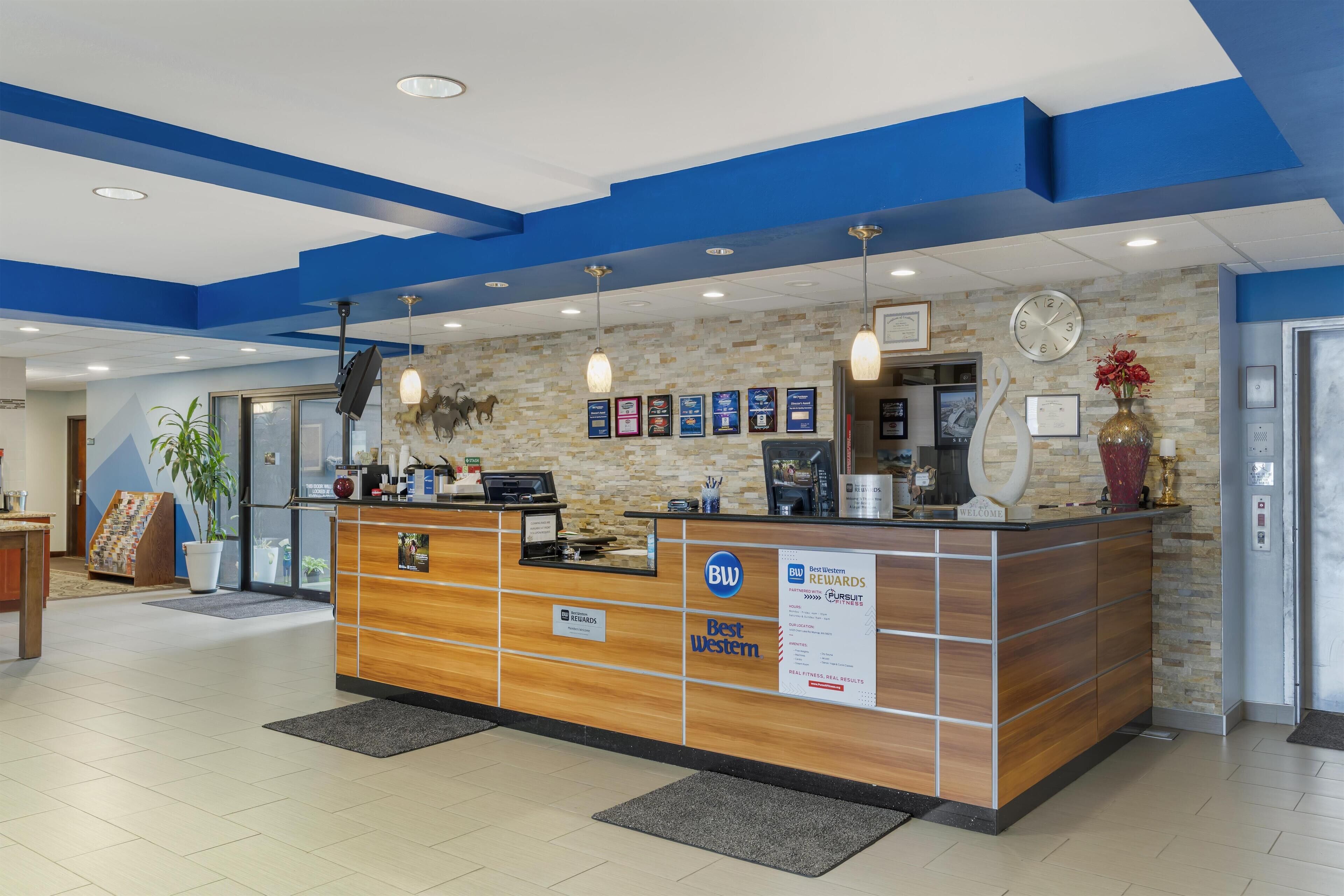 Un mostrador de recepción con detalles de madera, un reloj, reconocimientos enmarcados y un cartel de Best Western Rewards.
