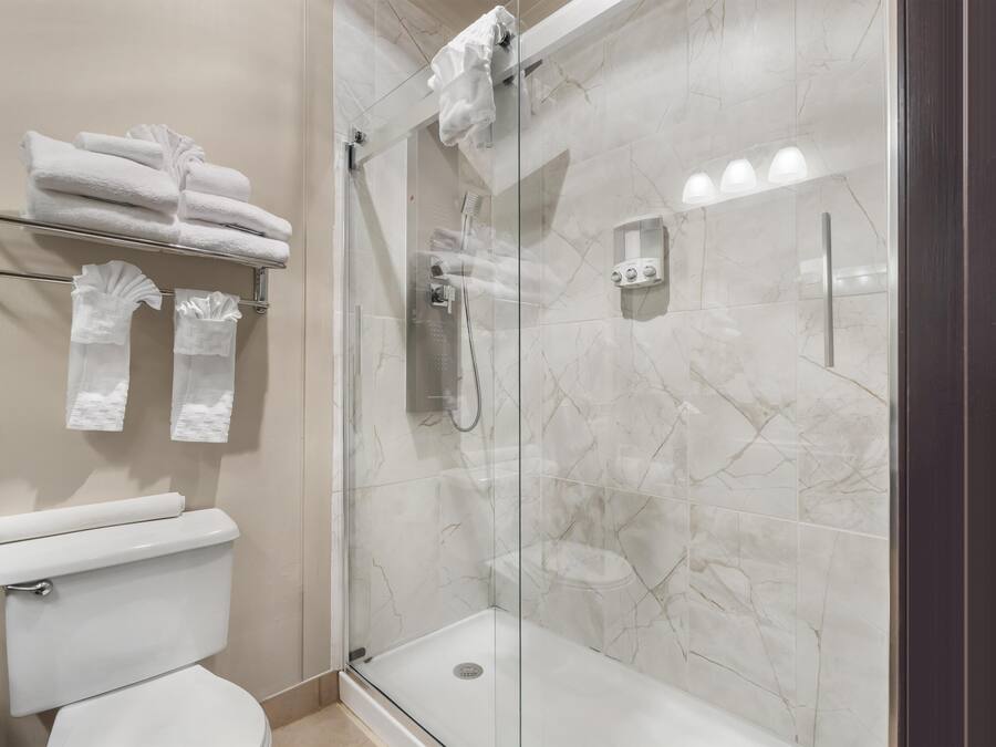 Un baño moderno con ducha de vidrio, inodoro y toallero con toallas dobladas.