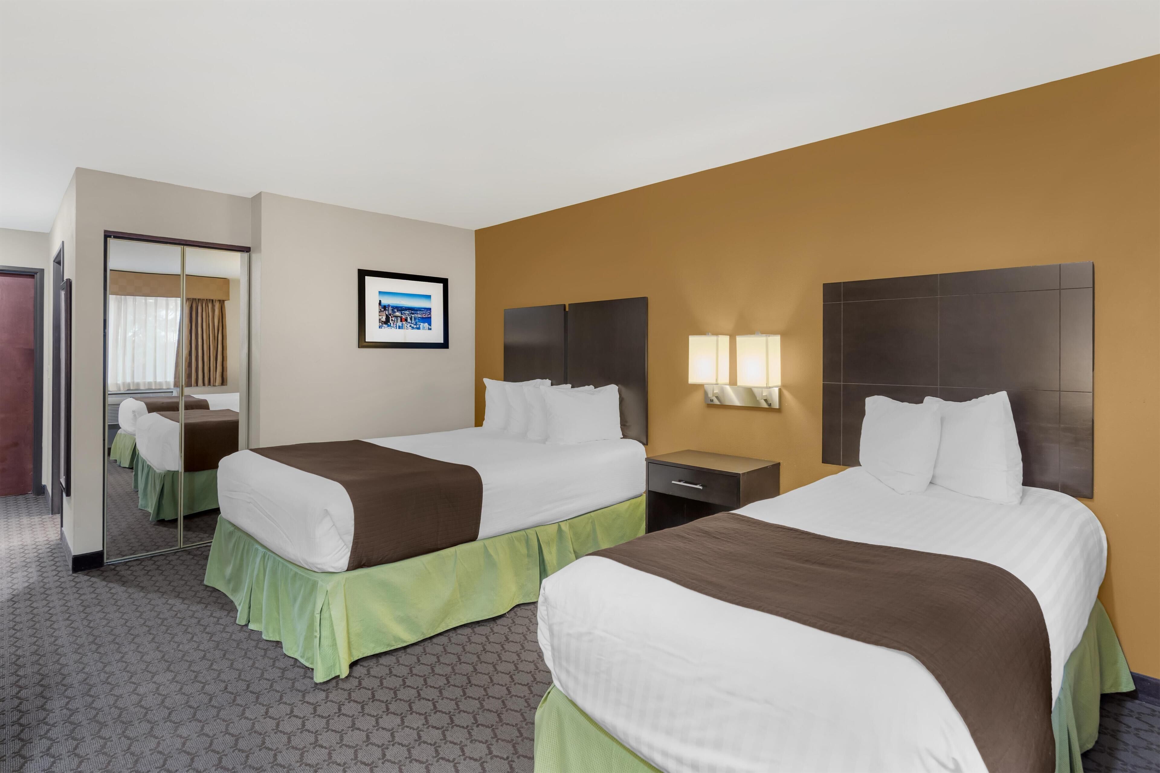 A hotel room with two beds, a mirror, a framed picture on the wall, and a nightstand with lamps.