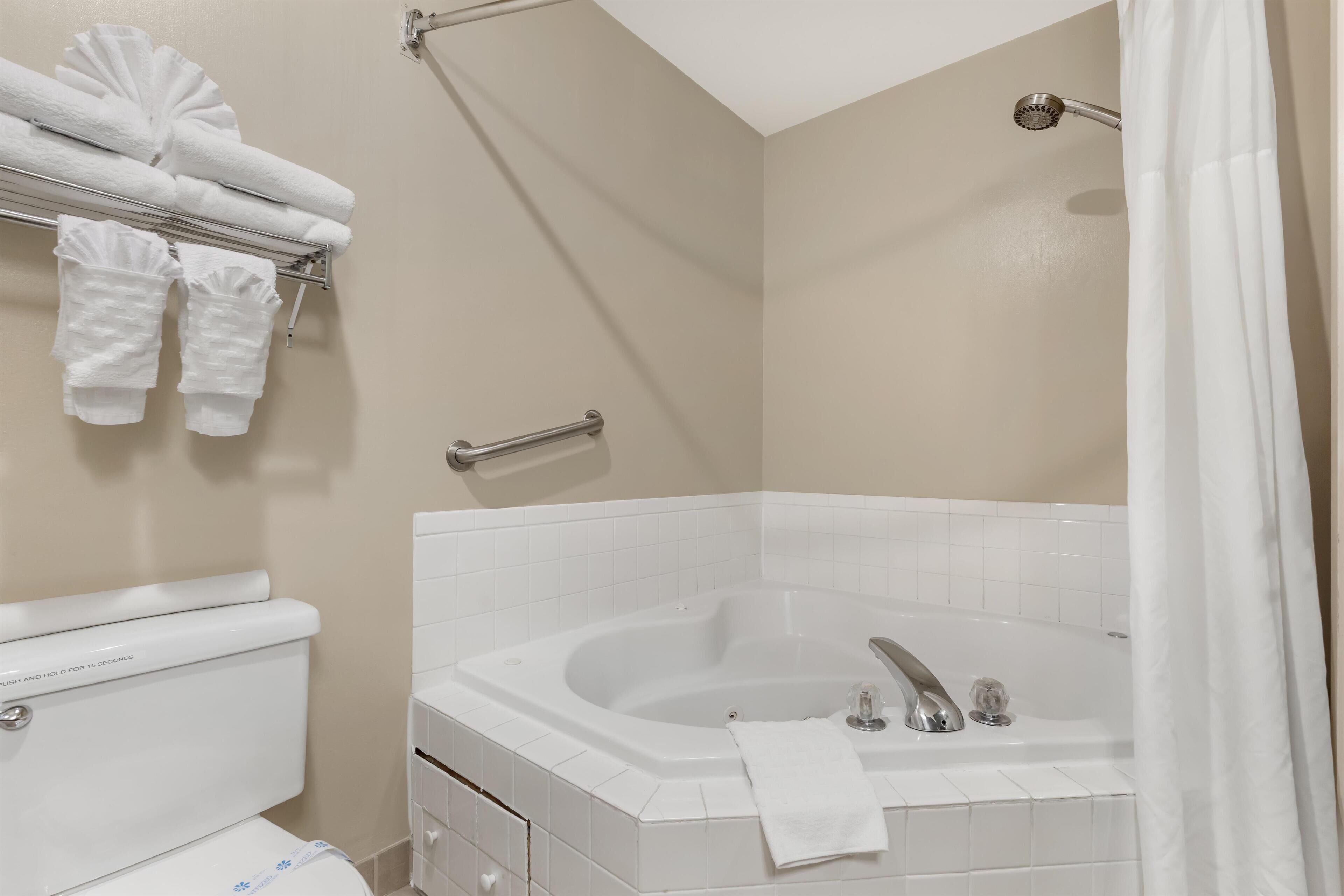 A bathroom with a white bathtub, a toilet, and a towel rack with folded towels.