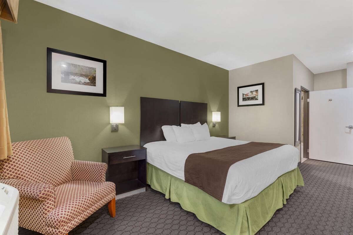 A hotel room with a bed, a chair, a nightstand, and two framed pictures on the wall.