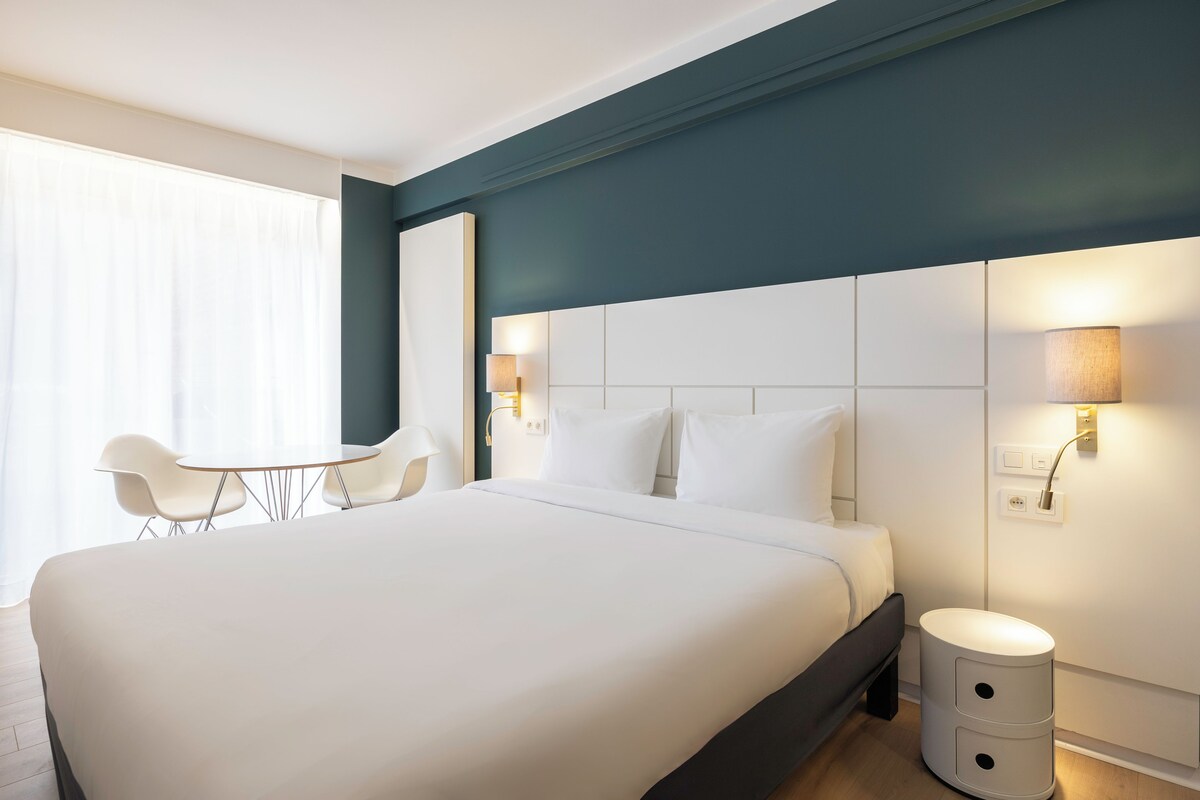 Une chambre d’hôtel moderne avec un grand lit, une table de chevet, une chaise et une lampe.
