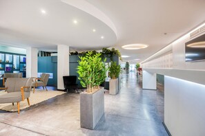 A modern lobby with a curved ceiling, seating area with patterned chairs, potted plants, and a reception desk. - Hotel Louise  (Brussels)
