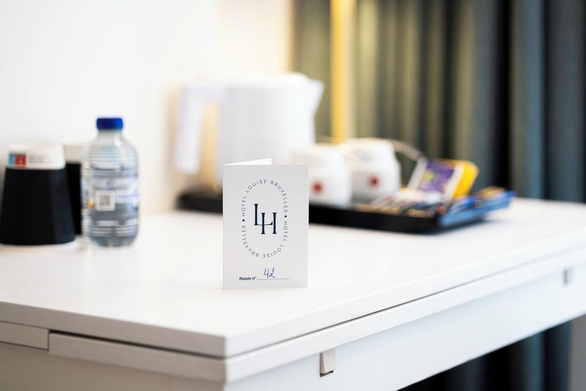 A hotel room with a white desk, a water bottle, a white mug, and a card with the number 4.