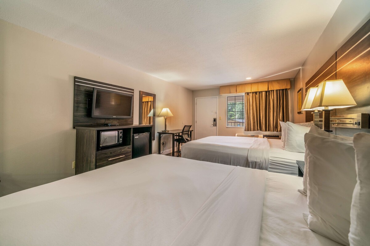 Habitación de hotel con dos camas, televisión, escritorio y ventana con cortinas.