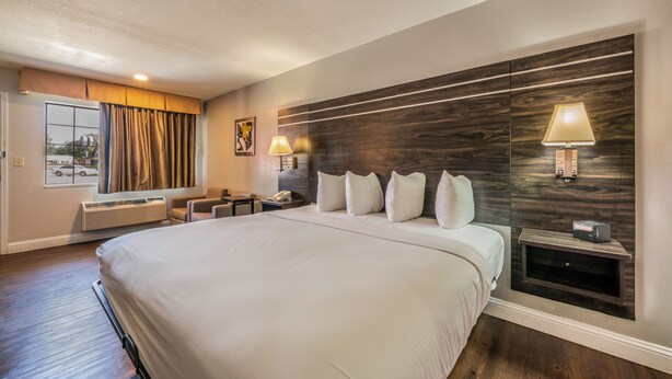 A large bed with a headboard, bedside lamps, a nightstand, a window with curtains, and a wall-mounted air conditioning unit. - Best Western Inn Of Jasper (Jasper)