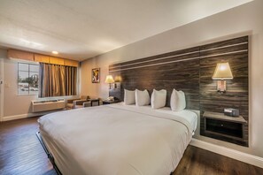 A large bed with a headboard, bedside lamps, a nightstand, a window with curtains, and a wall-mounted air conditioning unit. - Best Western Inn Of Jasper (Jasper)