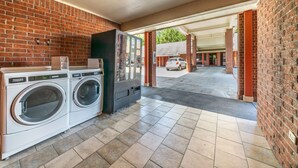 A laundry area with two front-loading washing machines and a dryer, a brick wall, and a covered walkway leading to a parking area. - Best Western Inn Of Jasper (Jasper)