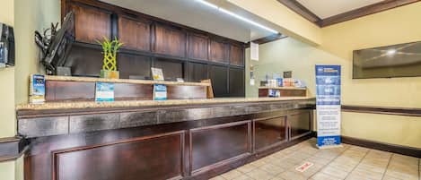 A reception area with a dark wood counter, a potted plant, and a signboard.