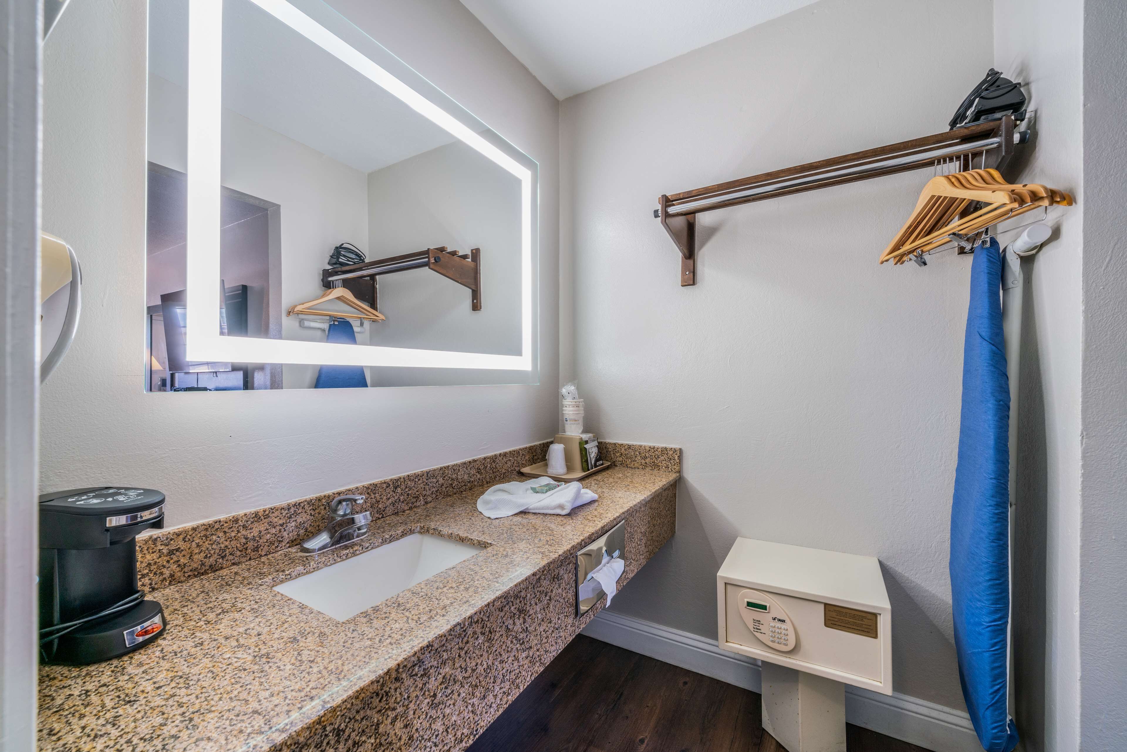 A bathroom with a granite countertop, a sink, a mirror, a towel rack, a shower curtain, and a control panel.
