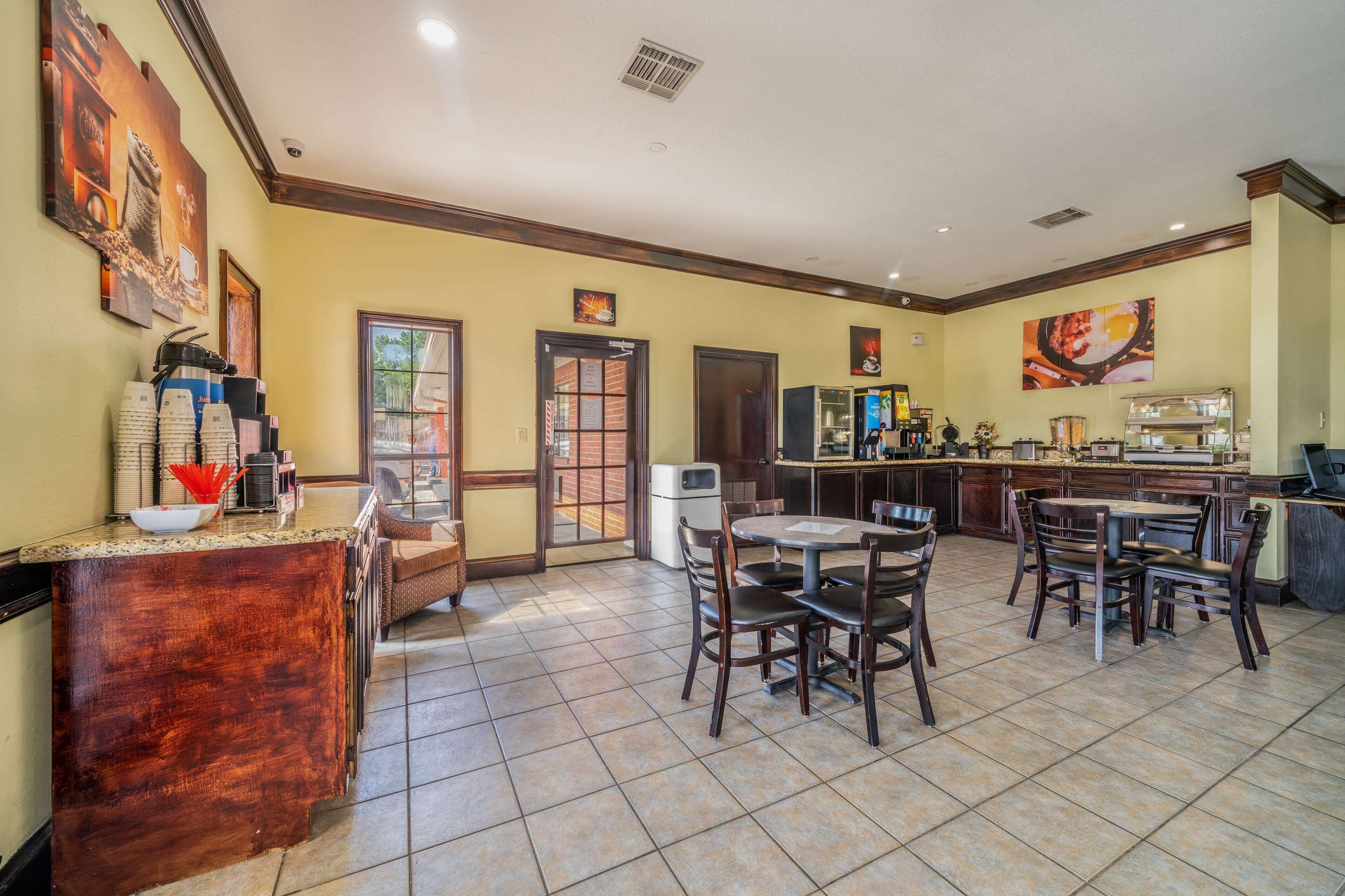 A spacious dining area with a central round table and chairs, a coffee station with multiple cups, and a kitchen area in the background.