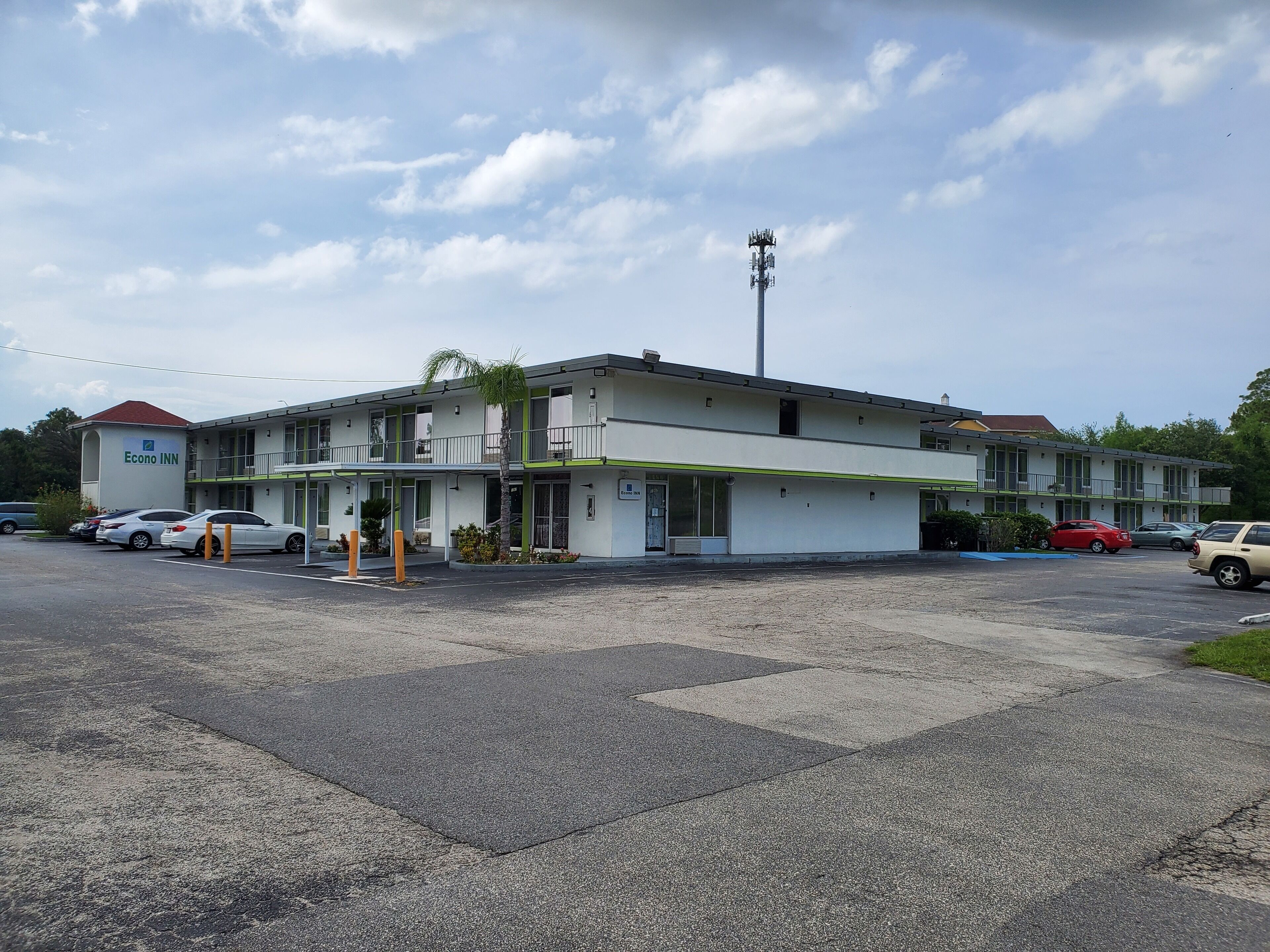A two-story motel with a green and white exterior, multiple balconies, and a parking lot with several cars.