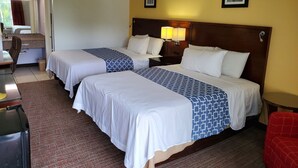 A hotel room with two beds, a desk, a chair, and a small table. - Econo Inn (Ormond Beach)
