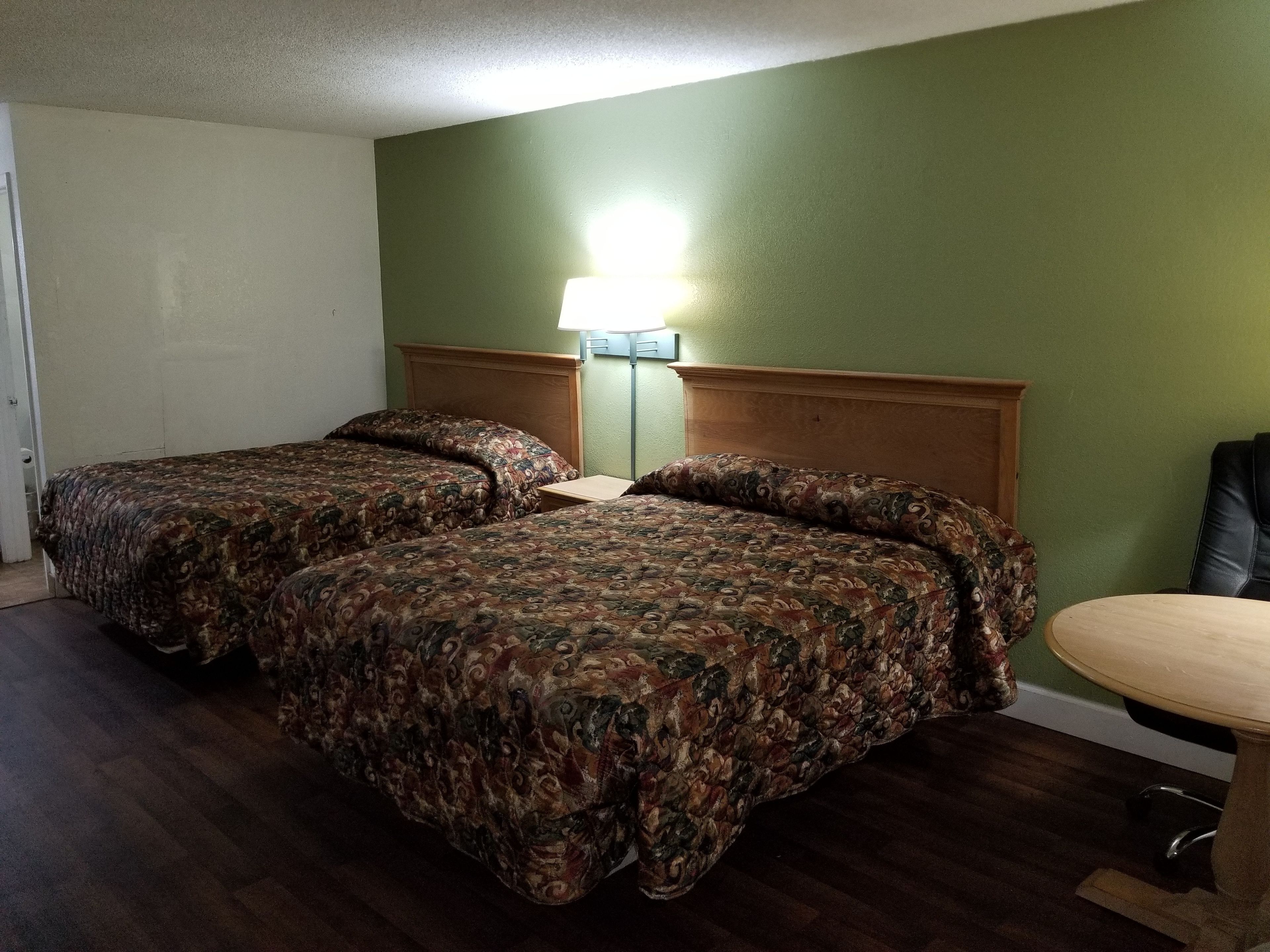 A hotel room with two beds, a wooden headboard, a green wall, and a small table.