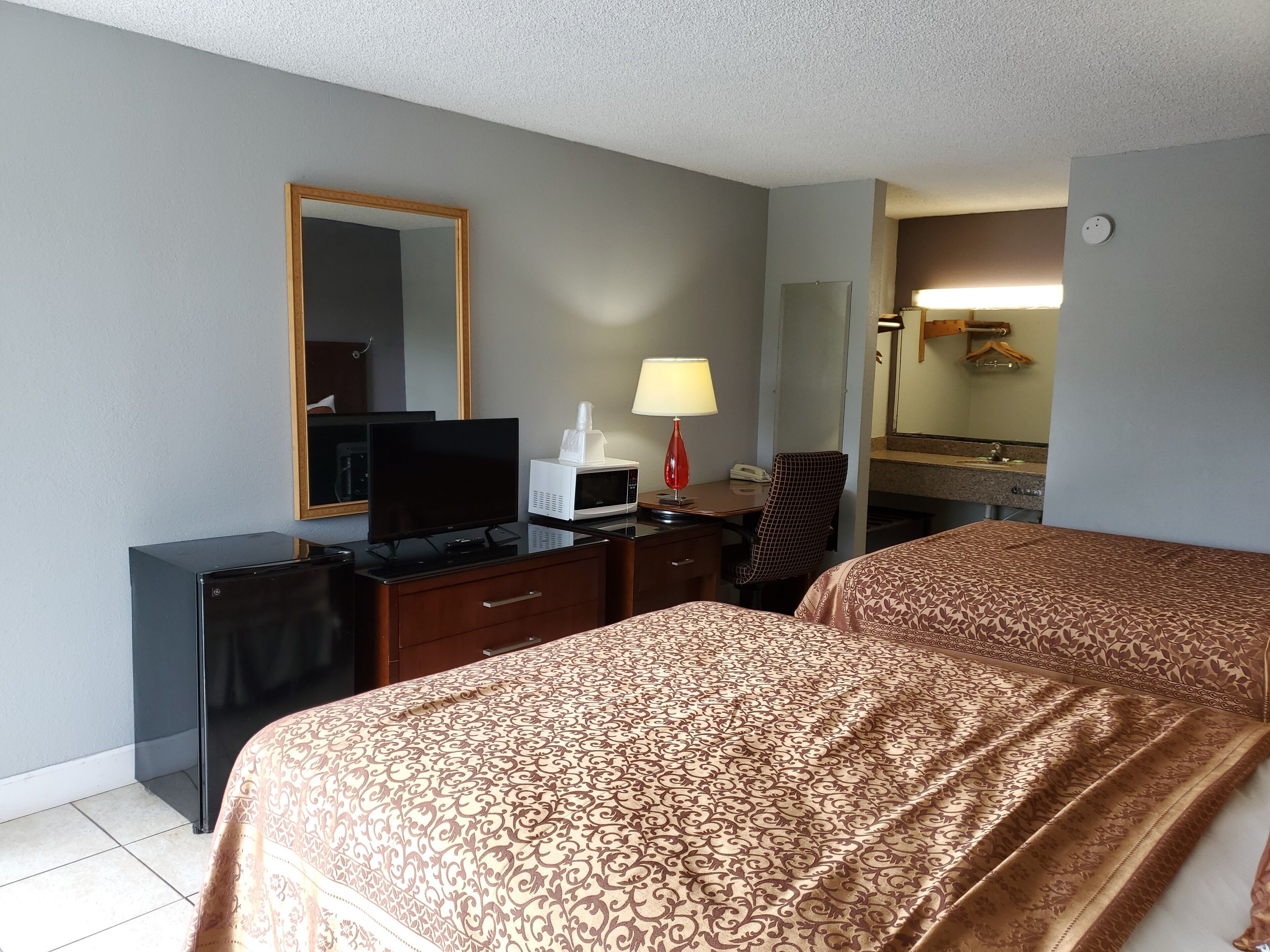 A hotel room with a bed, a desk with a computer, a television, a microwave, a lamp, and a mirror.