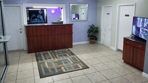 A living room with a wooden entertainment center, a television, a potted plant, and a patterned rug. - Econo Inn (Ormond Beach)