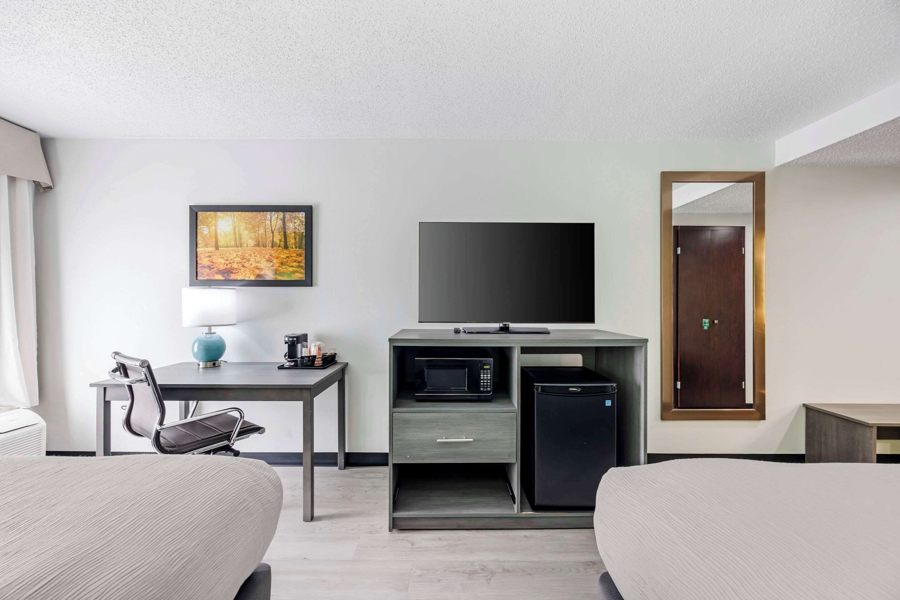 A hotel room with two beds, a desk with a flat-screen TV, a microwave, a small refrigerator, a lamp, and a painting on the wall.