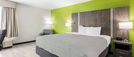 Una habitación de hotel con una cama grande, dos lámparas de noche, una mesita de noche con un reloj y una silla.