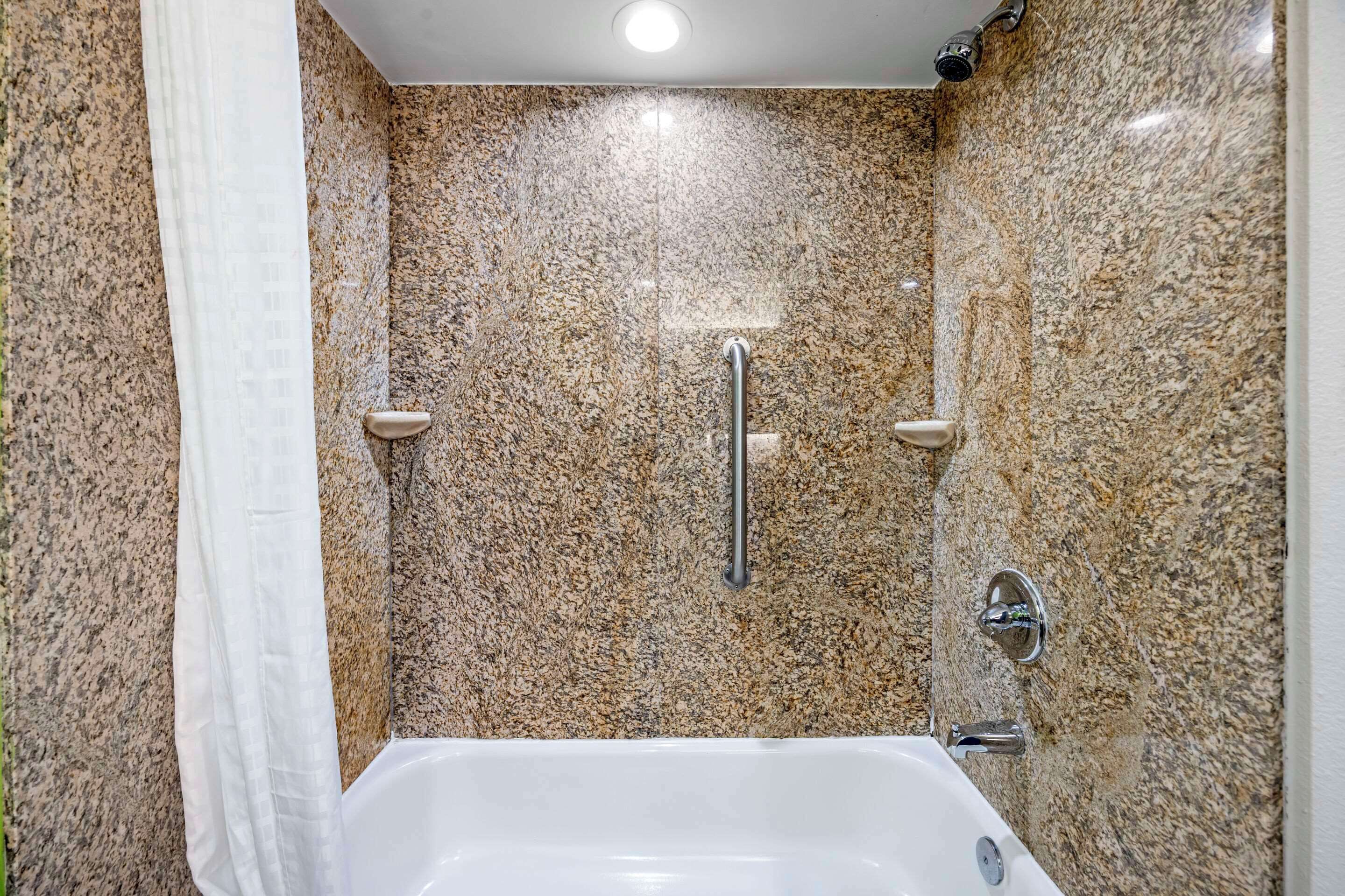 A bathroom with a white bathtub, granite walls, and a shower with a handheld showerhead.