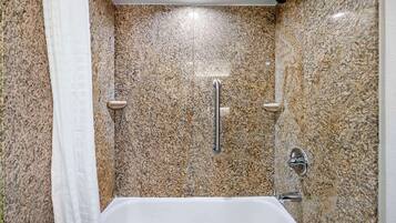 A bathroom with a white bathtub, granite walls, and a shower with a handheld showerhead.
