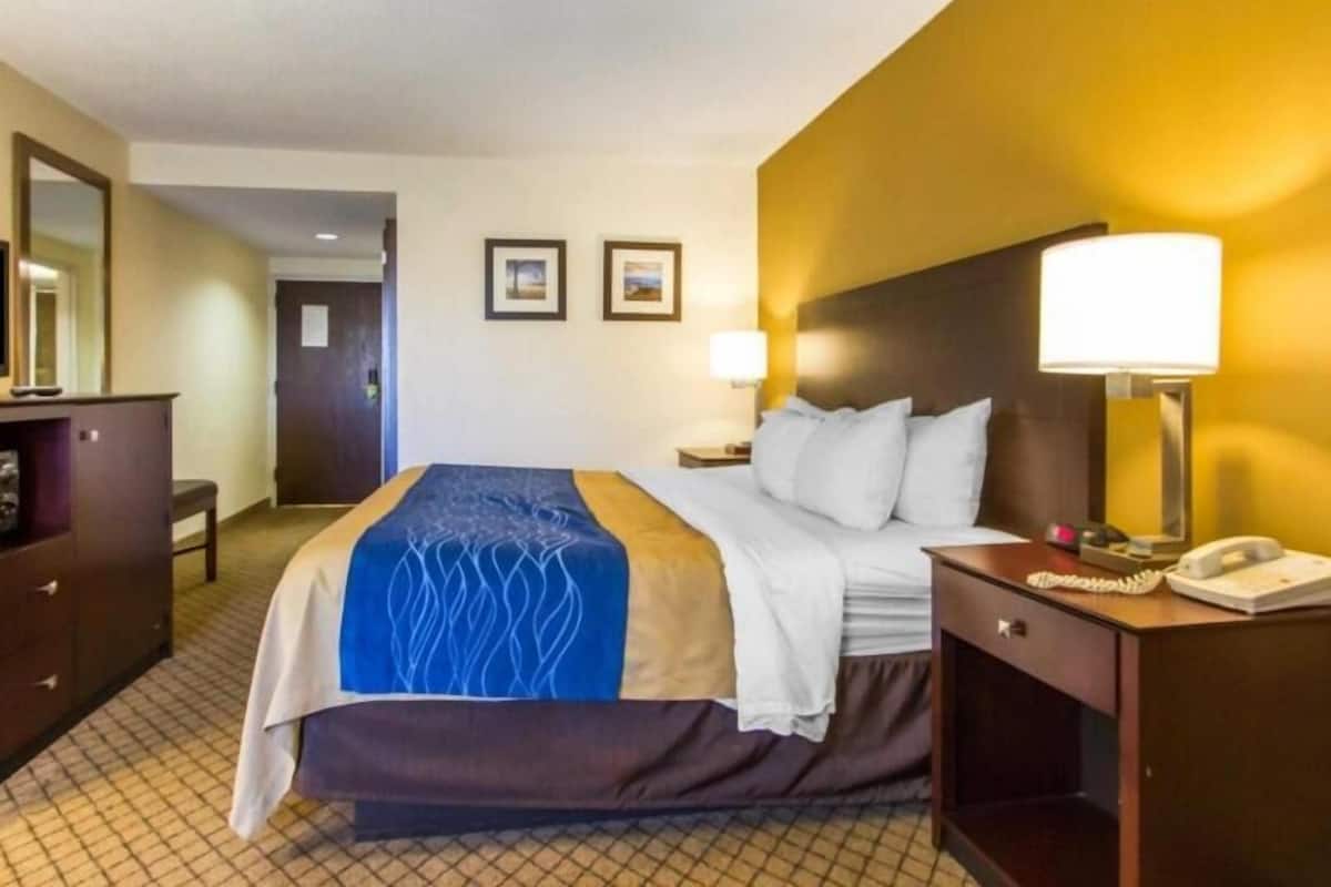 Ein Hotelzimmer mit einem Bett, Nachttisch, Lampe und einem Schreibtisch mit Telefon.