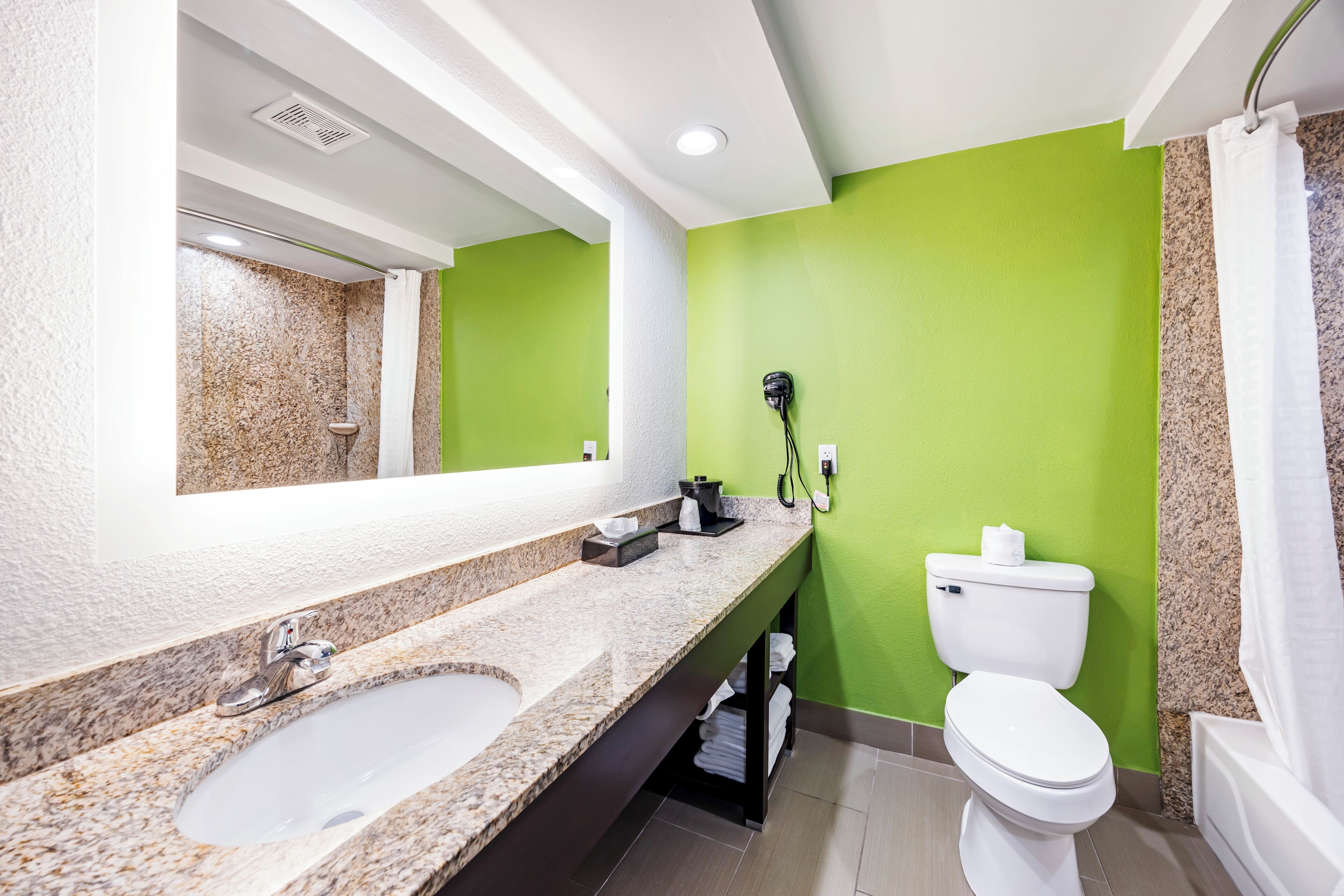 A bathroom with a granite countertop sink, a white toilet, and a green wall.