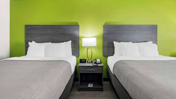 A hotel room with two beds, a nightstand with a lamp, a clock, and a phone.
