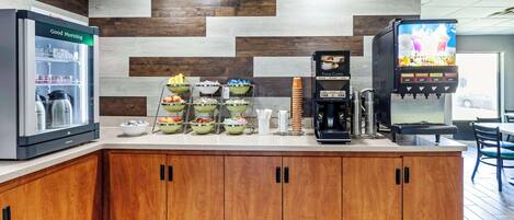 Una barra de desayuno con refrigerador, cafetera y televisor mostrando un menú de alimentos.