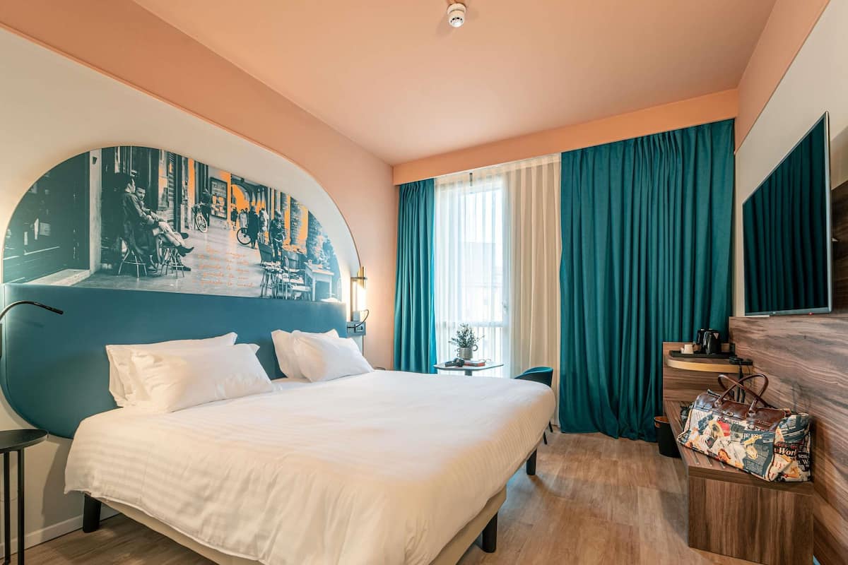 Ein Hotelzimmer mit einem großen Bett, einem Schreibtisch, einem Sessel, einem Fernseher und einem Wandregal.