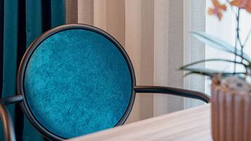 A room with a wooden table, a blue upholstered chair, and a vase with flowers.
