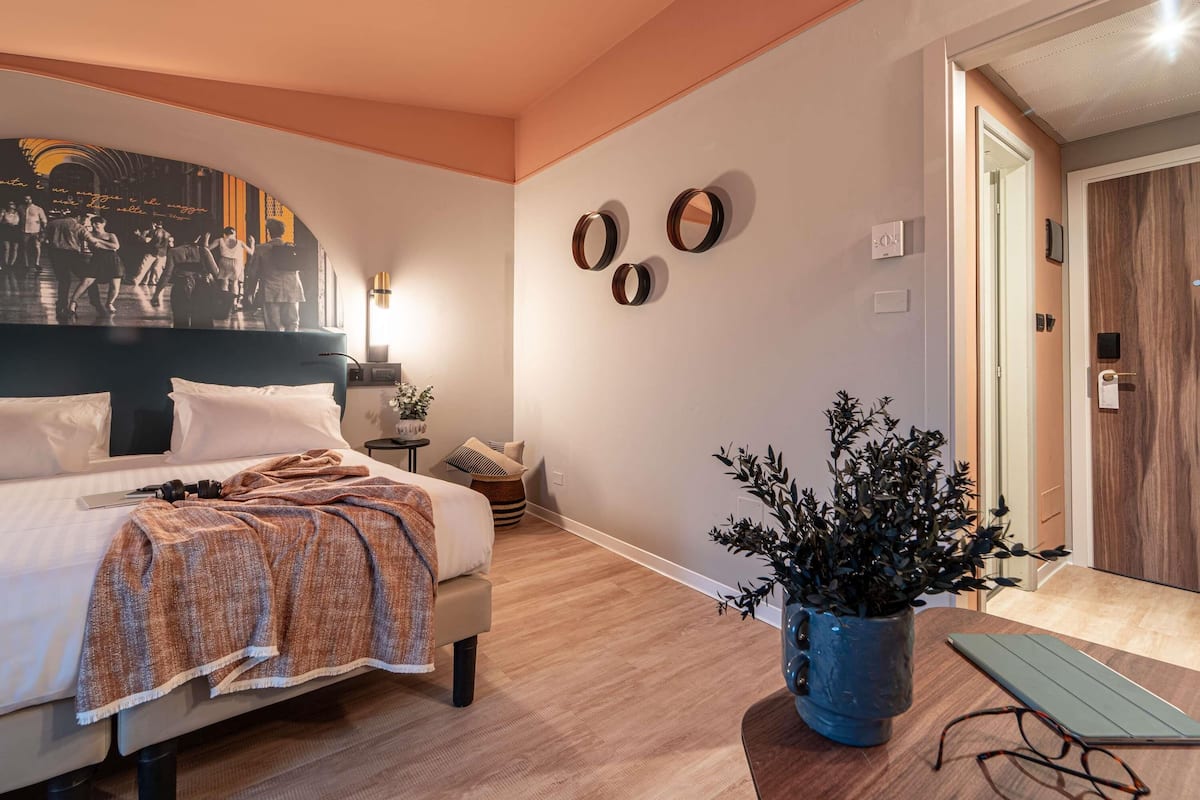 Ein modernes Schlafzimmer mit einem großen Bett, einem Wand-Fernseher, einem kleinen Beistelltisch und einer Topfpflanze.