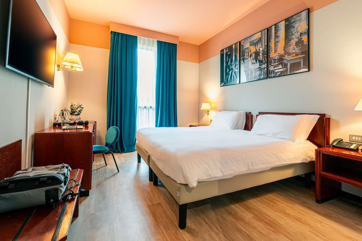 Ein Hotelzimmer mit Bett, Schreibtisch, Stuhl, Fernseher und einem Bild an der Wand.