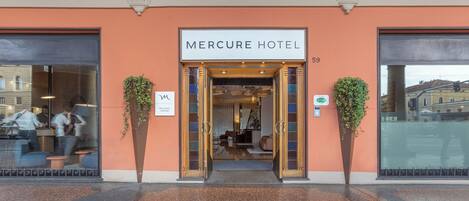 Exterior do Hotel Mercure, com entrada visível, uma placa de identificação e um vaso de planta de cada lado.