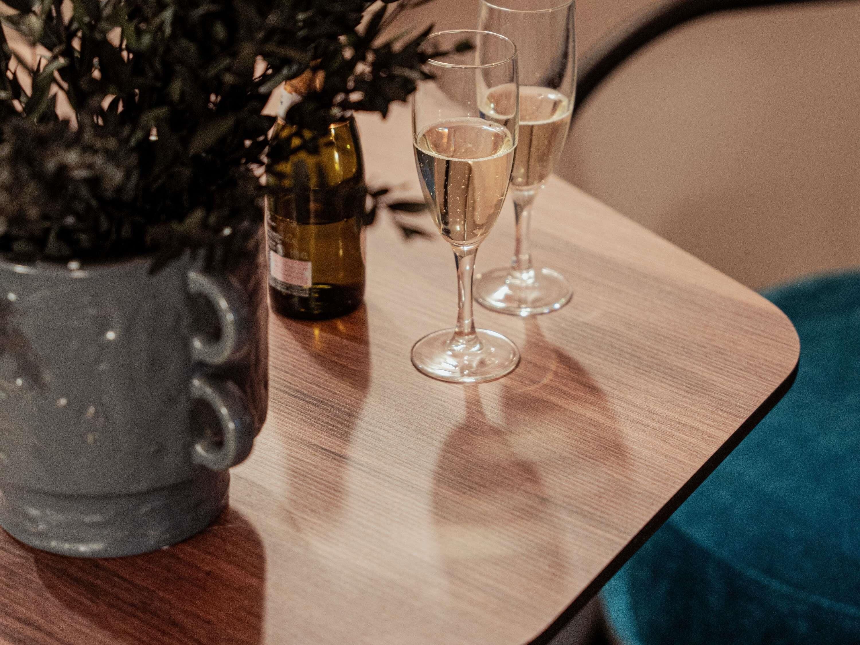 Een tafel met een fles wijn en twee glazen, een plant in pot en een blauwe doek.