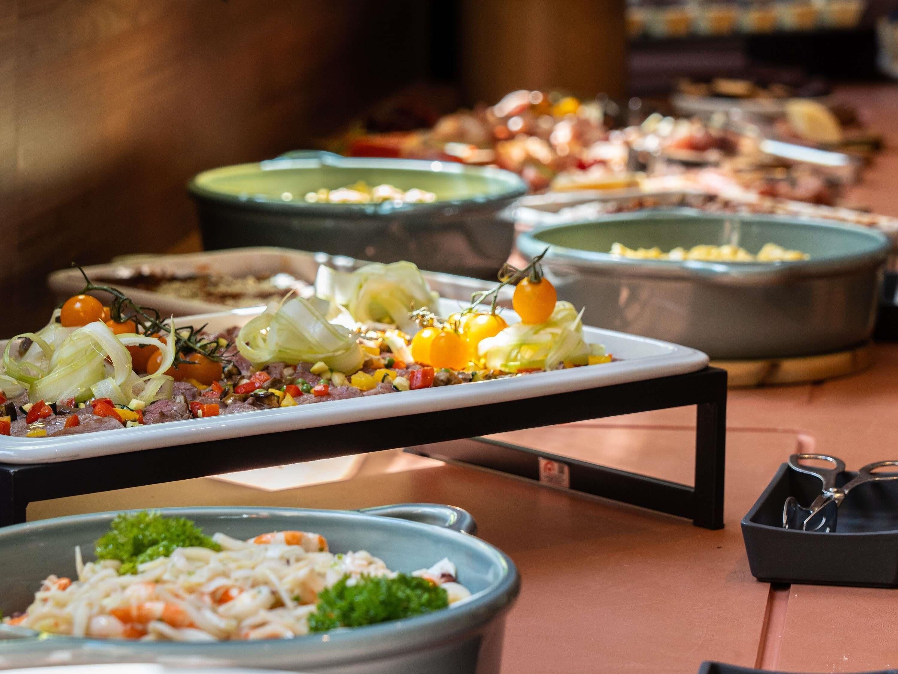 A buffet table with various dishes, including a plate with meat, vegetables, and garnishes.