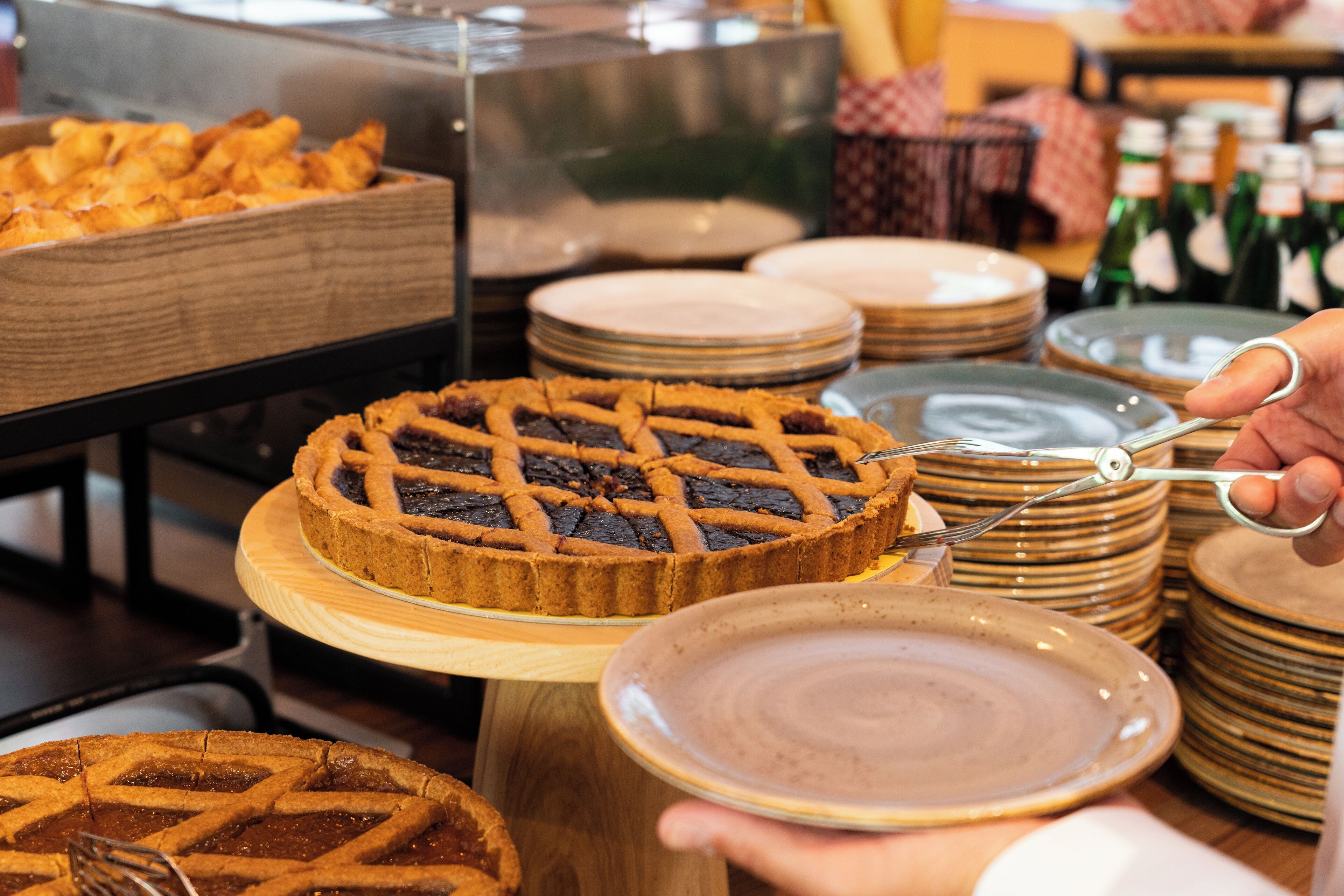 Variedad de tartas sobre pedestales de madera, con una persona cortando una tarta con tijeras.