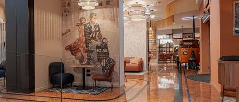 Un moderno vestíbulo de hotel con piso de mármol pulido, un área de descanso central y una pared con una gran obra de arte abstracto.