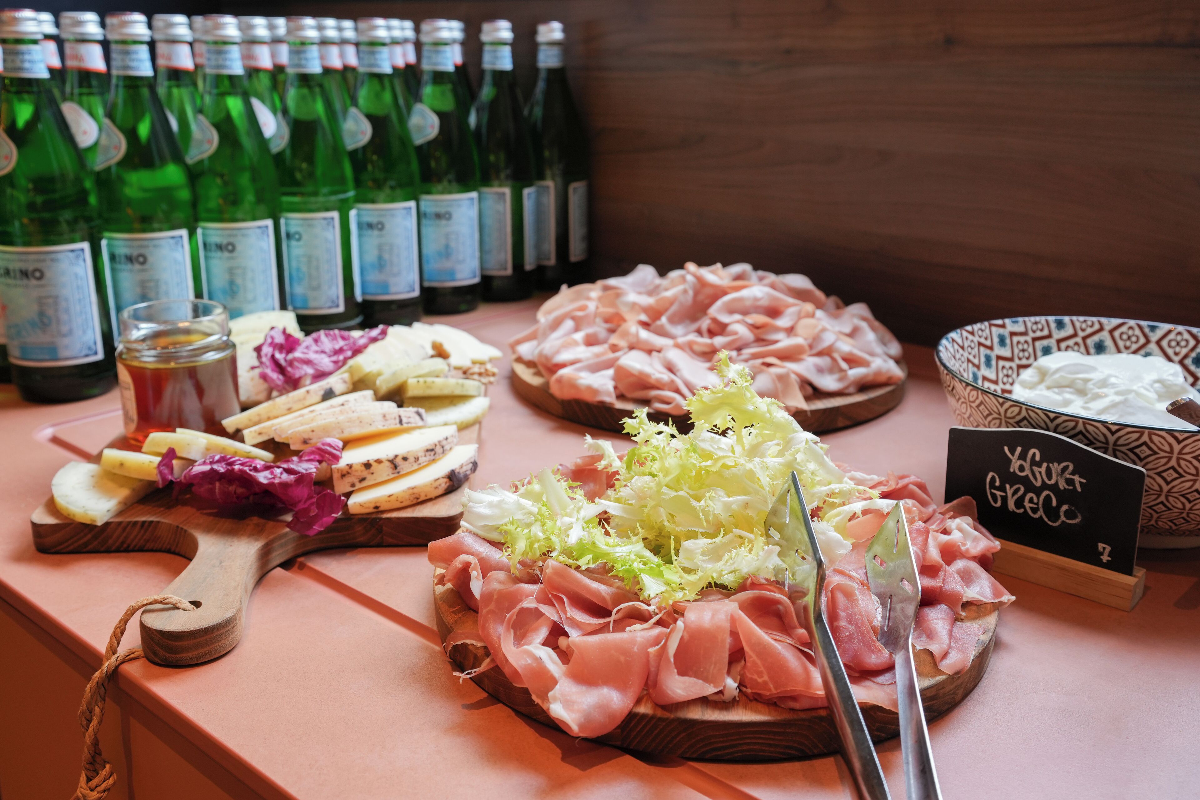 Eine Auswahl an Käse, Fleisch und eine Schale Joghurt auf einer Holzplatte.