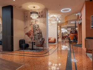 Un moderno vestíbulo de hotel con una zona de estar central, un mostrador de recepción y un comedor.