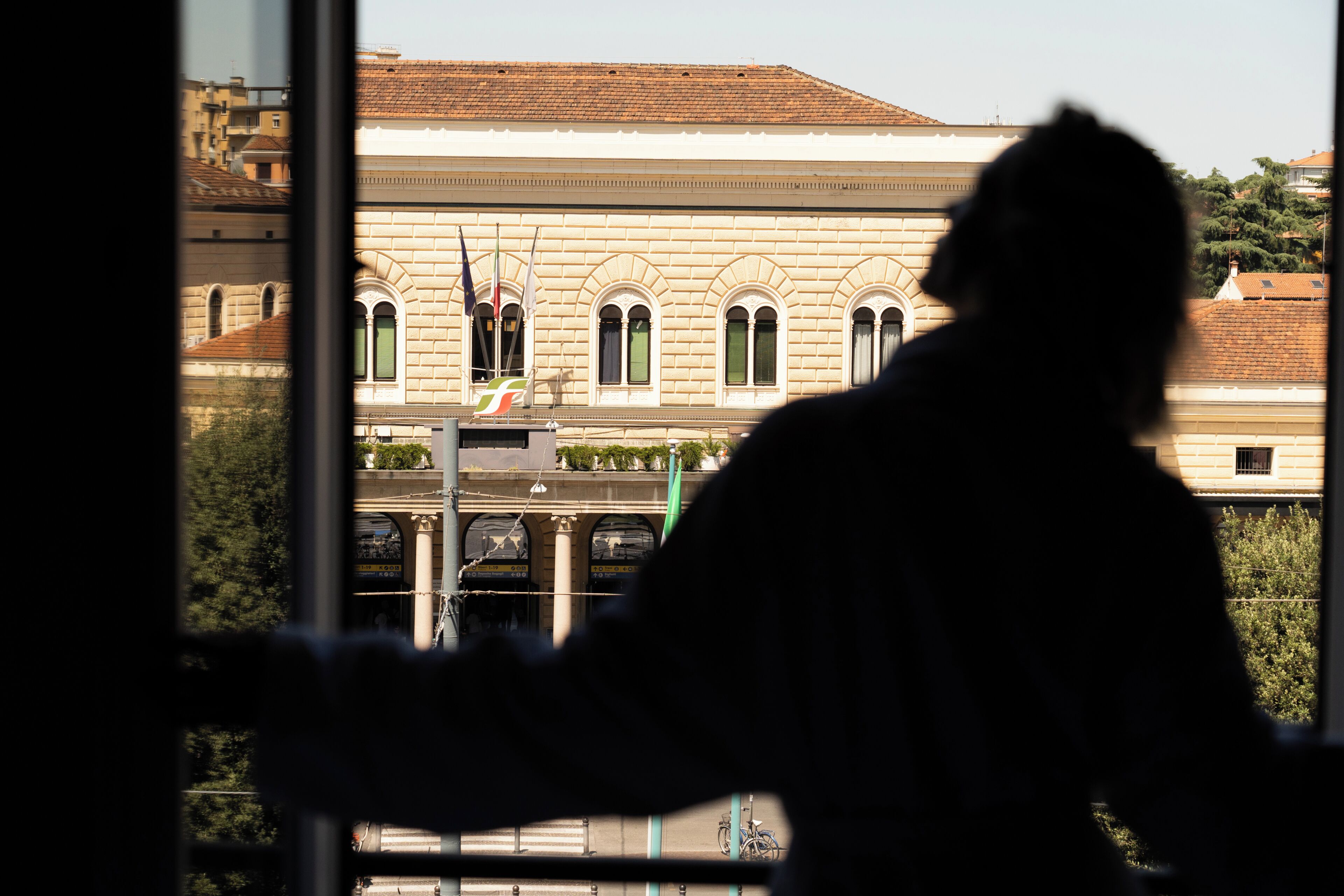 La silhouette d’une personne se tenant devant un bâtiment doté de fenêtres en arc de cercle et d’un toit recouvert de tuiles.