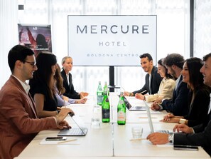 A conference room with a large sign reading 'MERCURE HOTEL' and 'BOLOGNA CENTRO' at the front.