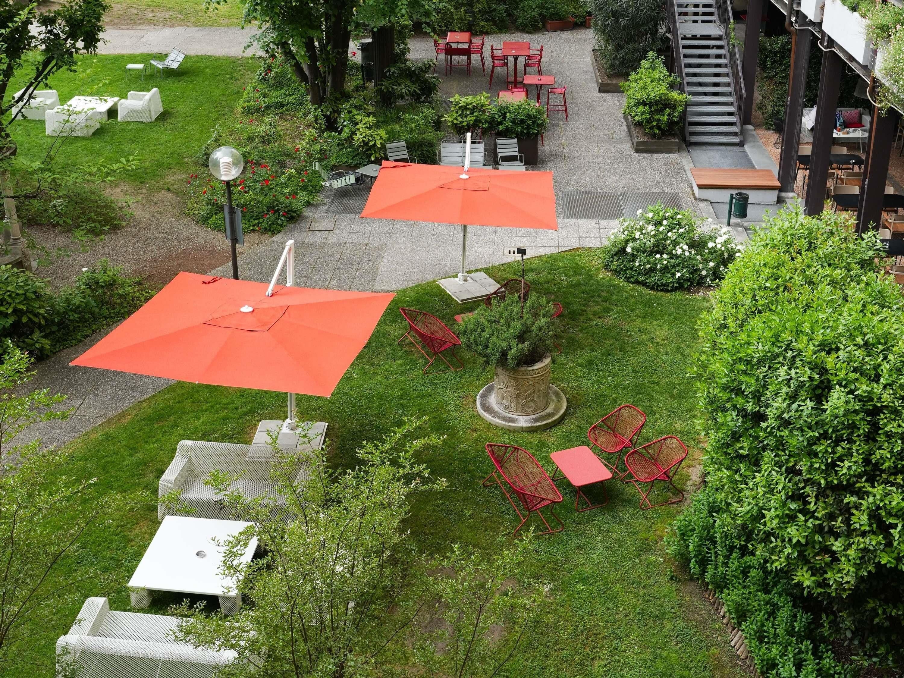 Un patio al aire libre con mesas y sillas, rodeado de follaje y un árbol pequeño.