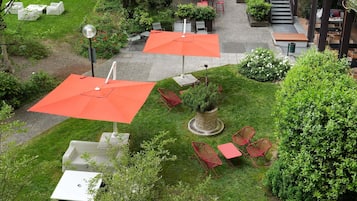 Un patio al aire libre con mesas y sillas, rodeado de follaje y un árbol pequeño.